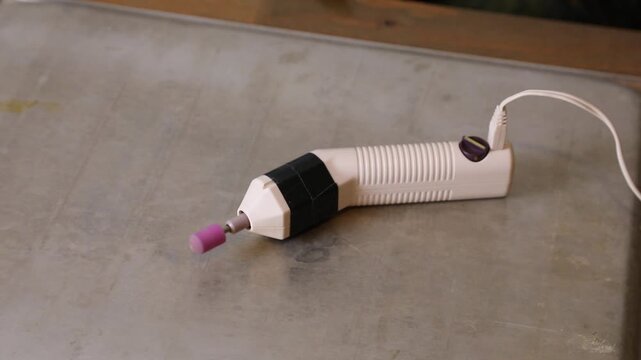 Electric nail drill machine with a pink grinding bit resting on a rustic metal surface