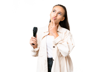 Young singer woman picking up a microphone over isolated chroma key background having doubts while looking up