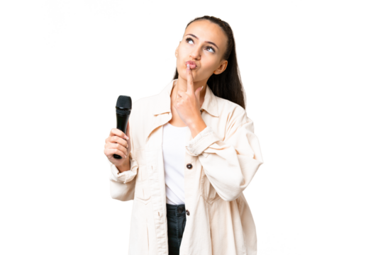 Young singer woman picking up a microphone over isolated chroma key background having doubts while looking up - Powered by Adobe