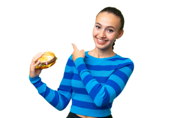 Young Arab woman holding a burger over isolated background pointing back