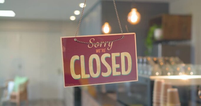 Worker walking into frame toward closed sign, flipping sign to open coffee shop