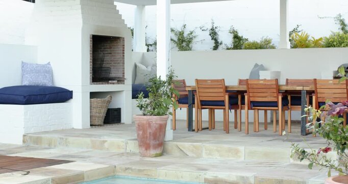 Camera is panning right across patio to showcase barbecue grill, cushioned bench and dining table