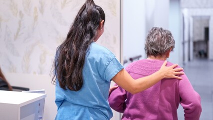 Granddaughter assisting elderly grandmother walking in nursing home