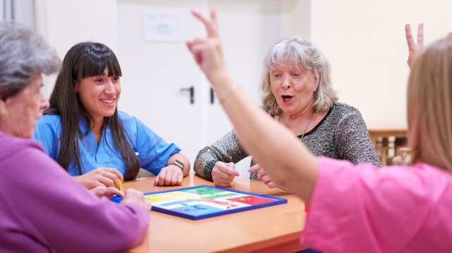 Seniors and caregiver playing board game in nursing home