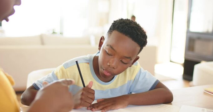 Mother passing pencil triggers African American boy writing homework at study table