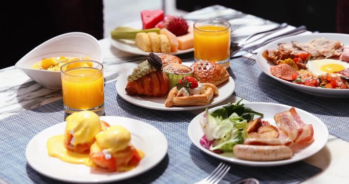 Gourmet breakfast spread with pastries, eggs benedict, fresh fruit, orange juice on elegant table. Brunch variety in restaurant setting.