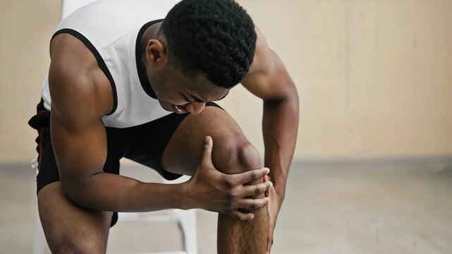Athletic young man experiencing sharp knee pain and discomfort while exercising indoors signaling injury or strain needing attention