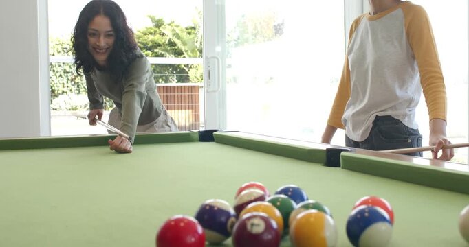 Diverse female friends chalking cues breaking rack of balls on pool table to start friendly match