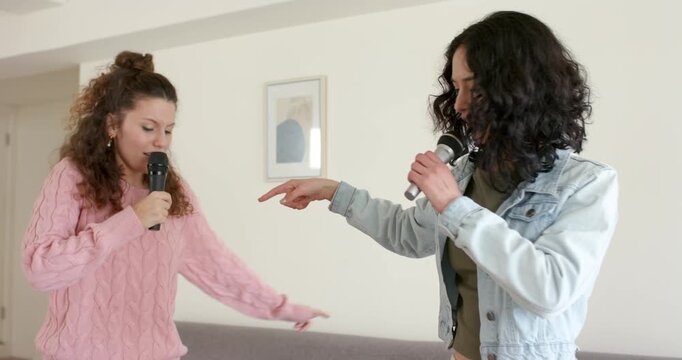 Hispanic and Asian friends starting verse with mics, singing, pointing, dancing in living room