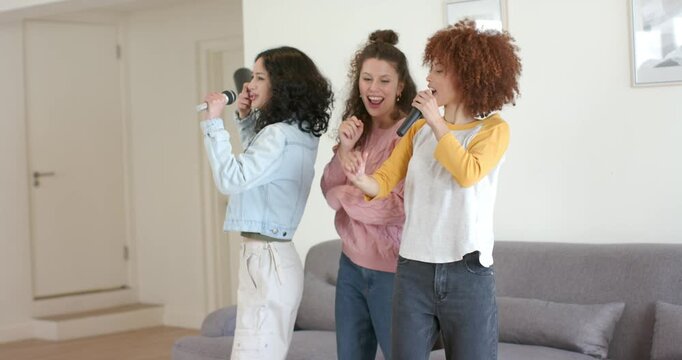 Three women friends singing into silver black mics in living room, music starting, switching leads