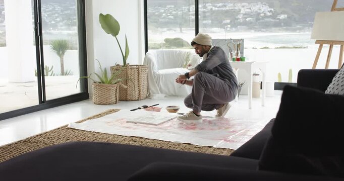 Male artist reaching for pink paint, dipping brush, covering canvas with abstract pattern in studio