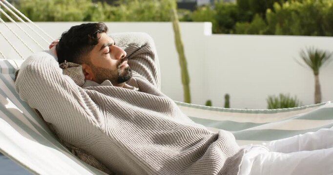 Inhaling, Indian man reclining, breathing in striped hammock on terrace with cushion for relaxation