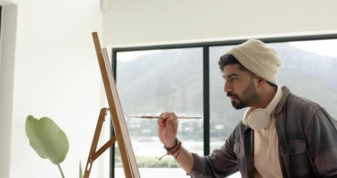 Blank canvas driving man mixing hues, painting strokes at studio window overlooking mountain town