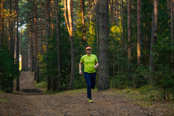 Obraz premium Man running a path through a sunlit pine forest, actively exercising in nature, maintaining physical fitness and health during an autumn outdoor training session