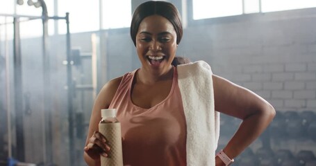 Finishing workout African American woman walking gym holding water bottle, cooling, adjusting towel - Powered by Adobe