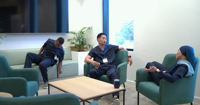 Diverse team talking in lounge, Asian man with cup gesturing, rising colleague handing phone