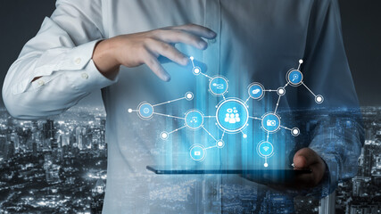 A business professional interacts with a digital tablet, illustrating advanced technology and social networking against a glowing city skyline under night sky. Tessel