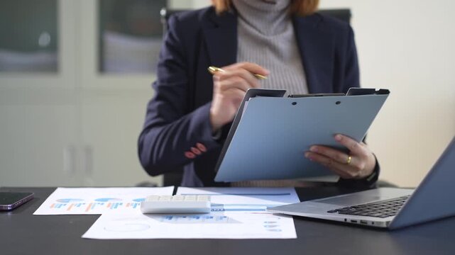 Female businessman working on desk office with using a calculator to calculate the numbers, finance accounting concept.