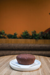 Close-up image of a round chocolate dessert served on a white ceramic plate placed on a wooden table.