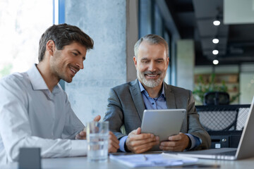 Mature businessman using a digital tablet to discuss information with a younger colleague in a modern business office