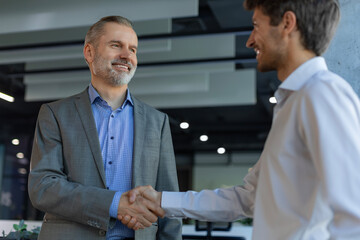 Business partners handshaking over business objects on workplace.