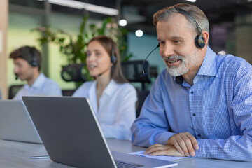 Smiling friendly handsome middle aged male call centre operator. Colleagues on the background
