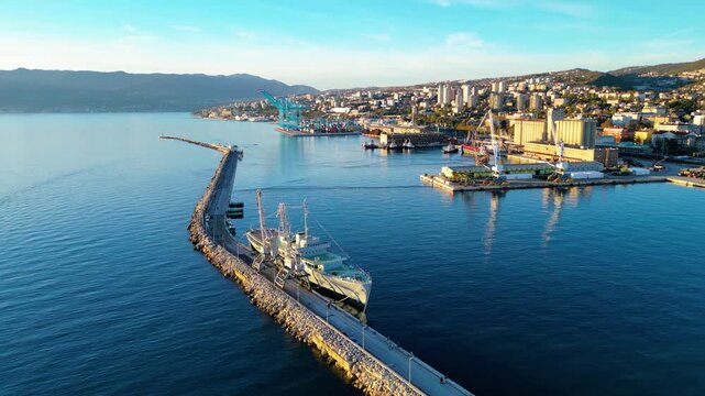 Golden hour light bathes Rijeka's bustling port and historic Molo Longo, Vessel Galeb, Tito. A vibrant Croatian coastal city nestled against mountains, showcasing maritime life.