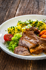 Baked veal cutlet with bone, boiled potatoes, mini carrots and green peas on wooden table