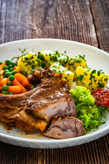Baked veal cutlet with bone, boiled potatoes, mini carrots and green peas on wooden table
