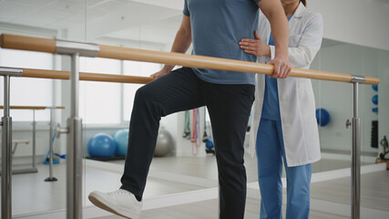 Physical therapist guiding patient taking step on parallel bars for rehabilitation and recovery