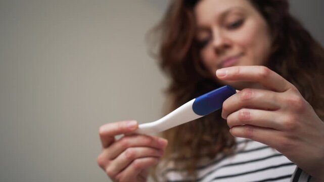 Hopeful young woman holding a pregnancy test and waiting for the result, her expression shifting from anticipation to a smile, symbolizing motherhood, fertility, and new beginnings