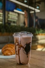 Iced Chocolate Drink in Plastic Cup with Croissant on Table