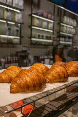 Fresh baked croissants displayed on rack in modern bakery interior