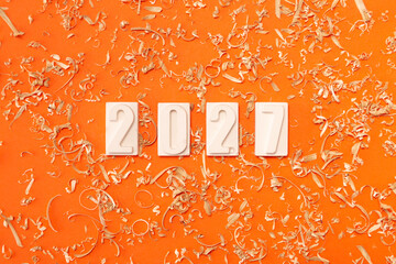 Сlose-up of the white numbers 2027 on a orange background with sawdust