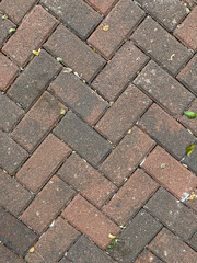 Close-up texture of red brick and dark gray concrete paver flooring arranged in a diagonal herringbone pattern.
