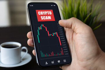 Male hand holding phone with chart scam crypto coins screen