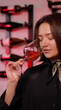 Professional sommelier woman testing rose wine aroma, holding a glass and evaluating characteristics in a wine tasting cellar