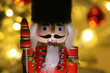 Close-up of a classic wooden nutcracker soldier in festive red uniform, set against warm holiday lights.