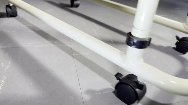 Closeup of the lower part of a trolley on wheel castors being slowly moved along an indoor washable vinyl tiled floor.