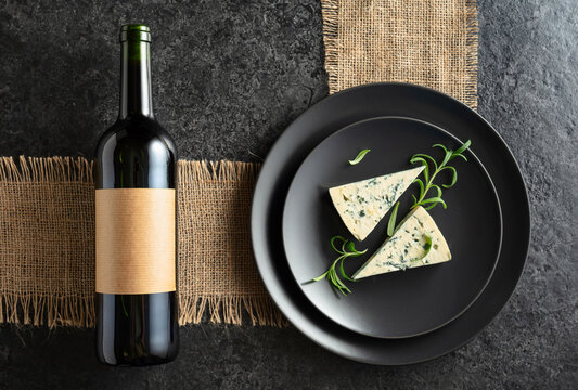 Bottle of red wine and blue cheese on a black plate.
