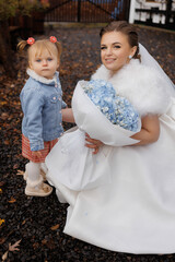 Beautiful bride holding bouquet with young girl in a cozy outdoor setting during fall