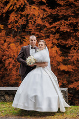 Fototapeta premium Couple poses in formal attire amid autumn colors, celebrating their wedding day