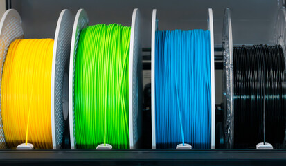 close-up of colorful 3D printer filament spools neatly arranged on a holder. Clean studio lighting and sharp details. Suitable for technology, manufacturing and 3D printing themes.