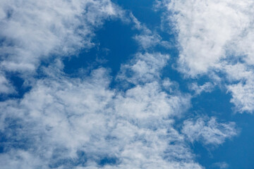 expansive, high-angle shot of a bright blue sky partially covered by scattered white, wispy cirrus and cumulus cloud formations. The composition, dominated by the vivid blue, offers a feeling of limit