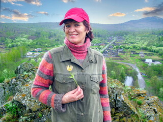A beautiful mature woman holds a snowdrop in her hands against the backdrop of the South Ural Mountains on a spring day