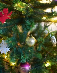 Close-up of decorated Christmas tree with glowing lights, shiny gold and purple baubles, and white snowflake ornaments. Festive holiday atmosphere with cozy warm lighting and natural pine texture.