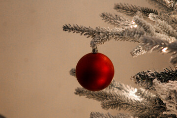 Close-up of a red Christmas ornament hanging from a snow-covered tree branch, creating a simple and elegant holiday atmosphere.