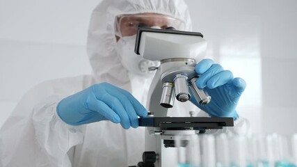 Scientific researcher wearing protective gear adjusting microscope, analyzing lab samples with precision in sterile research environment. Medicine, healthcare and science concept