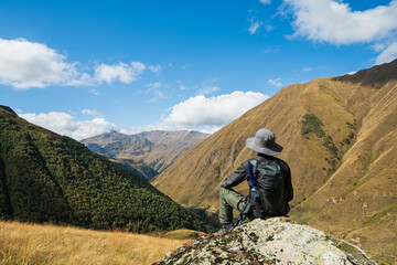 Traveler sitting on a rocky cliff overlooking dramatic mountains in Juta Village, Georgia. Peaceful hiking scene with stunning landscape and adventure travel inspiration.