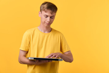 Young man in a yellow t shirt using a tablet against a bright yellow background, focused on the screen, casual technology use, modern learning and digital interaction